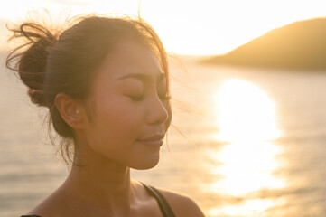 Young asian woman in sportswear doing yoga on the rock at seaside during Sunset, health and meditation concept