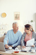 © Mediaphotos - Content gray-haired man in blue sweater sitting at coffee table with laptop in living room and discussing family budget with wife