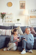 © Mediaphotos - Senior brown-haired woman in glasses sitting on carpet in living room and chatting with husband while drinking wine
