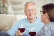 © Mediaphotos - Content handsome elderly man with wineglass listening to wife while enjoying romantic time with loved person