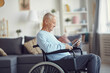 © Mediaphotos - Content disabled senior man with gray hair sitting in wheelchair and using tablet to read online news