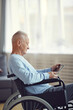 © Mediaphotos - Serious handicapped elderly man in casual sweater sitting in wheelchair and watching movie on digital tablet