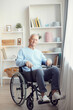 © Mediaphotos - Portrait of content disabled aged man with gray hair sitting in wheelchair in modern room with shelves in background