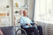 © Mediaphotos - Content pensive senior man in casual sweater and jeans sitting in wheelchair and looking out window while spending time at home