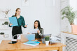 © klavdiyav - two young business women professionals in formal wear clothes work in modern office using laptop, tablet, brainstorm and search for solutions together, confident independent Asian girl solves problems
