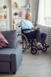 © Mediaphotos - Serious mature gray-haired man with paralyzed legs sitting in wheelchair by window and reading book