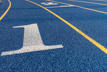 Close up lane number 1 on a new blue running track with yellow lane lines and other markings.