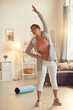 © Mediaphotos - Serious purposeful senior woman in leggings standing in living room and doing side bend exercise alone