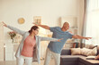 © Mediaphotos - Content senior couple in activewear standing in living room and outstretching arms while training together at home