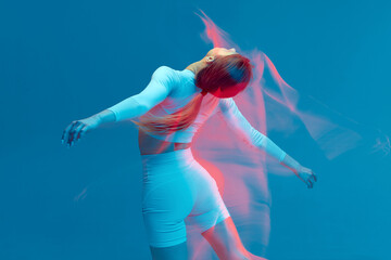 Sporty beautiful girl in white tracksuit dancing on blue background. Isolated fitness model in studio with motion blur effect.