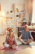 © Mediaphotos - Serene senior couple with crossed legs sitting on yoga mats in living room and meditating with closed eyes