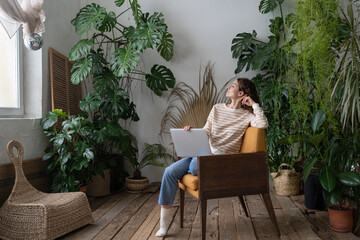 Wall Mural - Dreamy relaxed young woman rest after finished work on laptop computer look in window sit in comfortable armchair in home garden. Freelancer female take peaceful break for relaxation and stress relief