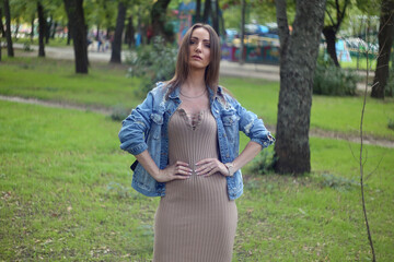 beautiful fashionable blond girl adult  posing in the park in dress and jeens jacket