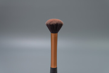 makeup powder brush gold and black on seamless gray background selective focus