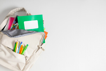 Backpack with colorful school supplies on white background. Back to school. Flat lay, top view, copy space