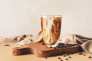 Wall Mural - Board with glass of cold brew and coffee beans on color table against light background