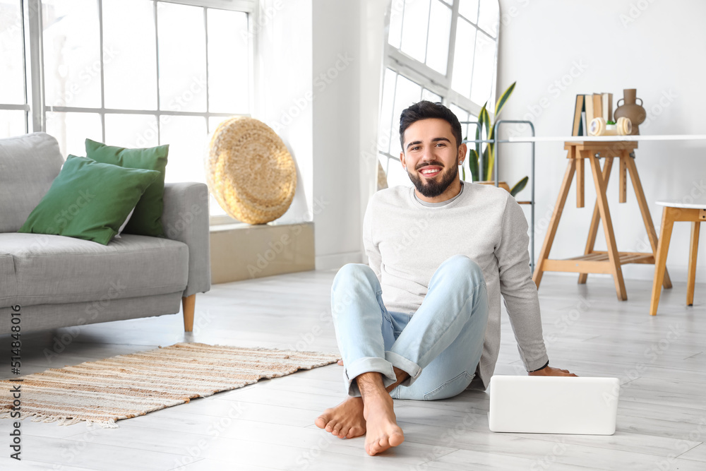 Handsome barefoot man with laptop sitting on floor at home