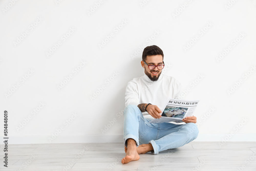 Handsome barefoot man reading newspaper near light wall