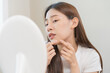© KMPZZZ - Dermatology, puberty asian young woman, girl looking into mirror, allergy when wear mask and cosmetic, show squeezing pimple spot for removing from face.Beauty care from skin problem by acne treatment