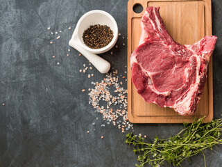 Raw cowboy steak with seasonings on stone background, rib eye on bone.