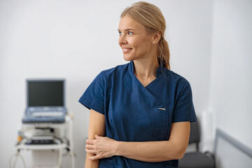 Wall Mural - Smiling doctor, ultrasound specialist looking at side on her workplace in clinic