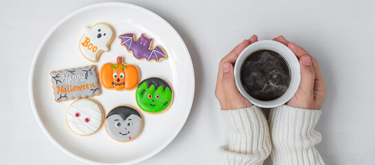 woman hand holding coffee cup during eating funny Halloween Cookies. Happy Halloween day, Trick or Threat, Hello October, fall autumn, Traditional, party and holiday concept