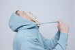 a tortured man suffering from problems with a mesh on his face stands in a light blue hoodie on a light background and pulls aside the lacing of the hoodie