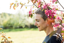Smiling Woman Standing By Branch Of Pink Flowers In Garden