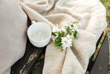 Cup Filled With Water Kept By White Flowers On Blanket On Bench