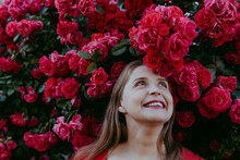 Happy Woman Standing Under Plant Of Red Roses