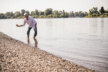 Playful Senior Man Throwing Pebbles In River