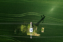 Transmission Tower Supporting Overhead Power Line Through Cultivated Crops Field, Aerial View From Drone Pov