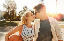 Summer Holidays, Love And People Concept - Happy Young Couple With Ball On Basketball Playground