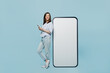 © ViDi Studio - Full size young happy woman she 30s in casual blouse big huge blank screen mobile cell phone with workspace copy space mockup area hold smartphone isolated on pastel plain light blue background studio