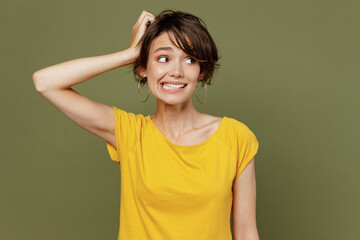 Wall Mural - Young confused minded sad woman she 20s wearing yellow t-shirt look aside on workspace area hold scratch head isolated on plain olive green khaki background studio portrait. People lifestyle concept.