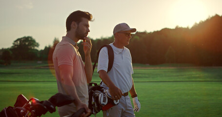 Wall Mural - Rich men playing golf on sunset summer course. Two players enjoy sport on field.