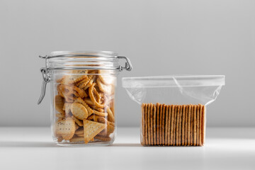 Wall Mural - food storage, eating and snacks concept - close up of salted cookies or crackers in jar and plastic bag on white table