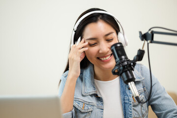 Wall Mural - Content creator woman host streaming her a podcast on laptop with headphones and microphone interview cheering guest conversation at broadcast studio. Blogger motivation recording voice over radio.