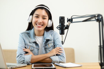 Wall Mural - Content creator woman host streaming her a podcast on laptop with headphones and microphone interview cheering guest conversation at broadcast studio. Blogger motivation recording voice over radio.