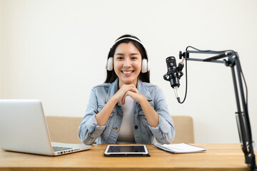 Wall Mural - Content creator woman host streaming her a podcast on laptop with headphones and microphone interview cheering guest conversation at broadcast studio. Blogger motivation recording voice over radio.