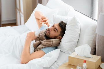 Wall Mural - people and health problem concept - unhappy sick man spraying his nose with nasal spray lying in bed at home