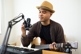 Fototapeta  - Professional Musician with condenser microphone and tablet for Mixing Mastering music. Hispanic male composing a song with guitar and piano keyboard at digital Recording home studio