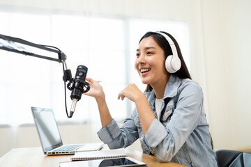 Wall Mural - Content creator woman host streaming her a podcast on laptop with headphones and microphone interview cheering guest conversation at broadcast studio. Blogger motivation recording voice over radio.