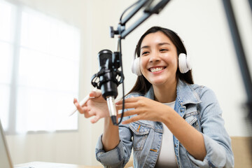 Wall Mural - Content creator woman host streaming her a podcast on laptop with headphones and microphone interview cheering guest conversation at broadcast studio. Blogger motivation recording voice over radio.