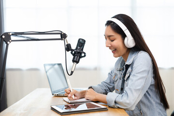 Wall Mural - Content creator woman host streaming her a podcast on laptop with headphones and microphone interview cheering guest conversation at broadcast studio. Blogger motivation recording voice over radio.