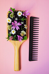 Wooden comb with a black comb on a pink background. Hairdressing tools for hair care with wildflowers. The concept of natural hair products