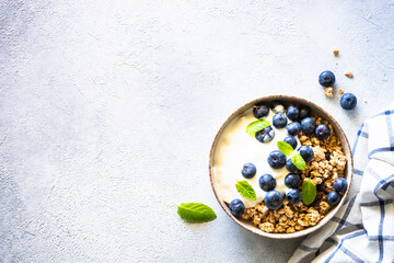 Wall Mural - Greek Yogurt with granola and fresh blueberries at light stone table. Top view with copy space.