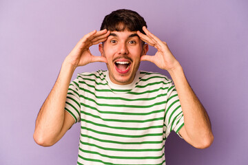 Wall Mural - Young caucasian man isolated on purple background receiving a pleasant surprise, excited and raising hands.