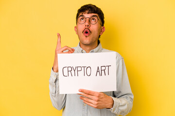 Wall Mural - Young hispanic man holding crypto art placard isolated on yellow background pointing upside with opened mouth.