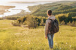 © Lyubov - Tourist with backpack standing on top of hill in grass field and enjoying beautiful landscape view. Rear view of teenage boy hiker resting in nature. Active lifestyle. Concept of local travel